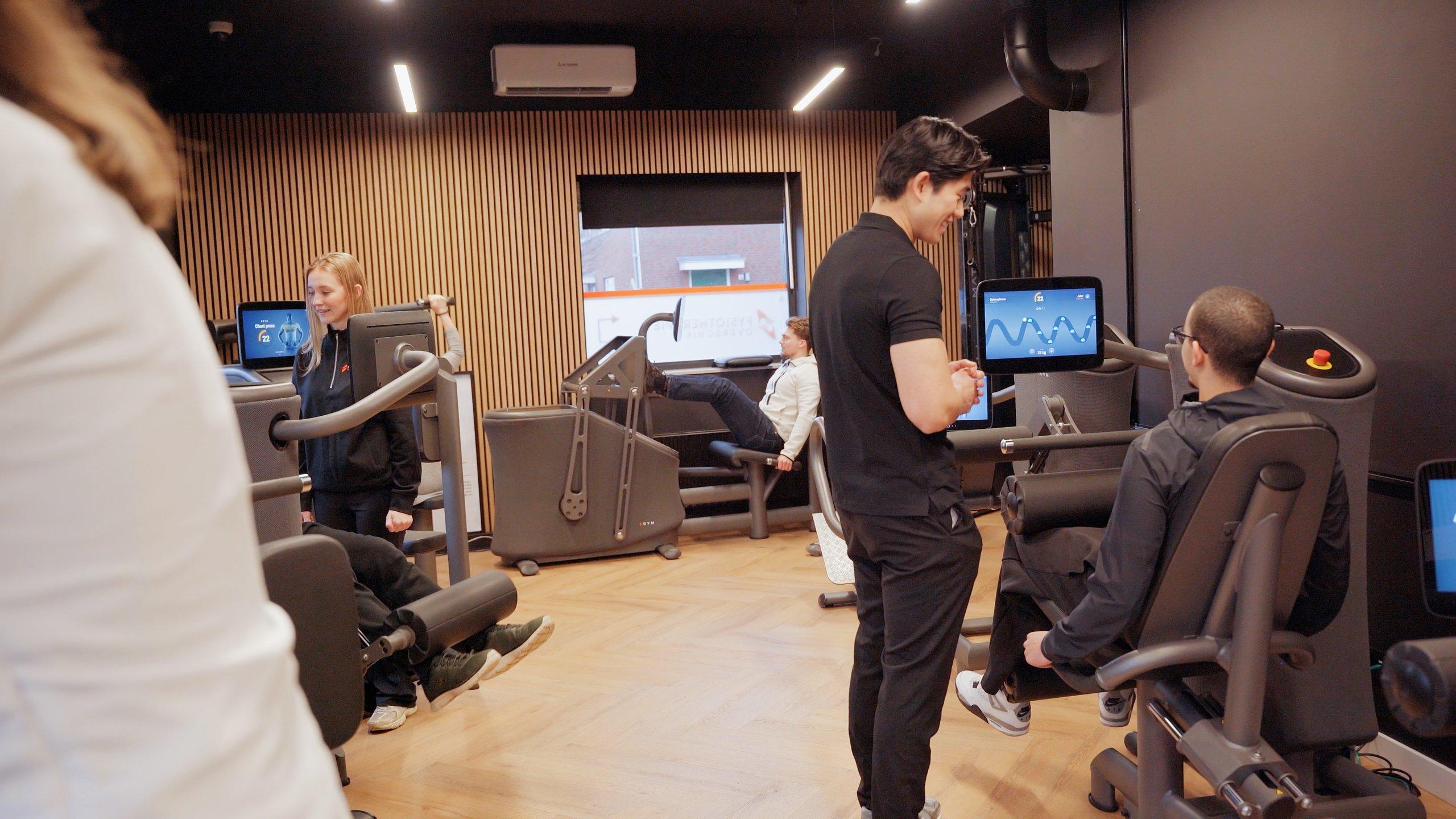 Een fitcoach begeleidt leden op de EGYM-toestellen in de sportruimte van Fysiotherapie Overschie